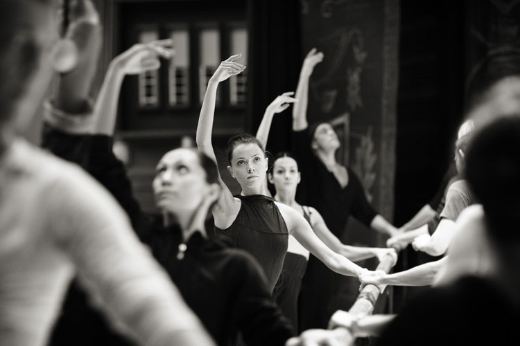 A black and white photograph of ballet dancers warming up by Helen Maybanks